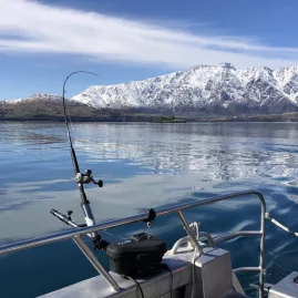 Fishing rod setup on a boat with calm Lake Wakatipu waters and The Remarkables in the background