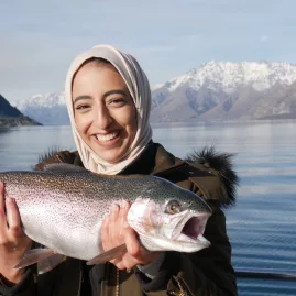 Woman holding a rainbow trout with Lake Wakatipu and snow-capped peaks in the background