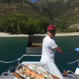 Man preparing cooked trout on a barbecue during a fishing trip on Lake Wakatipu