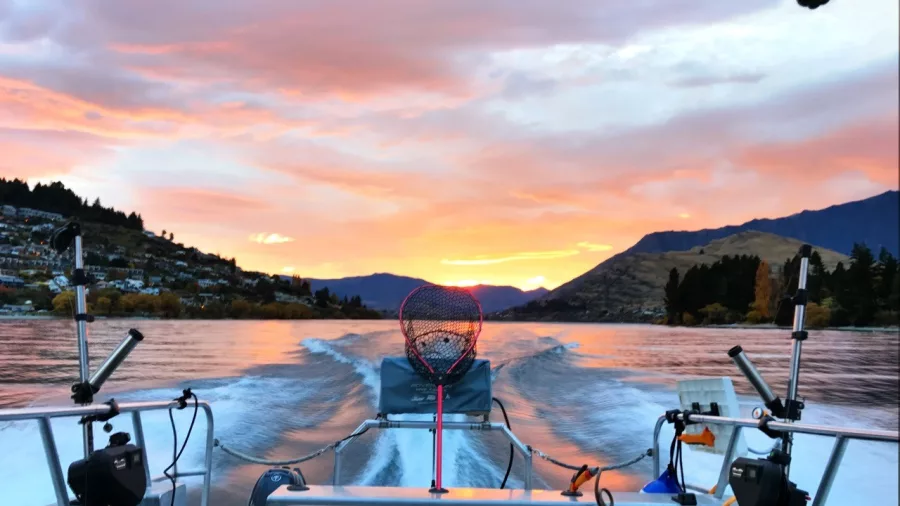 Fishing boat speeding across Lake Wakatipu at sunset with gear and mountains in view