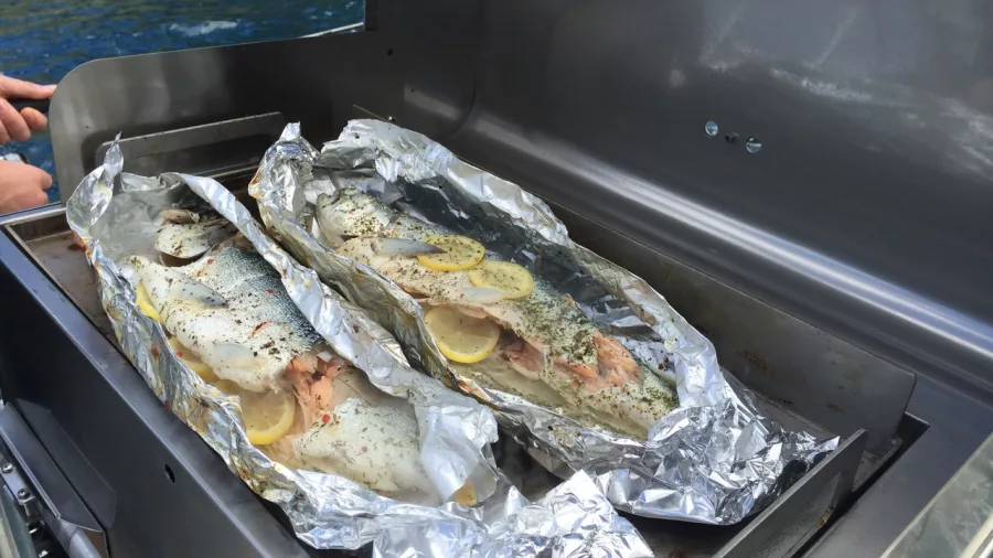 Two whole trout wrapped in foil with lemon, cooking on a barbecue on a fishing boat