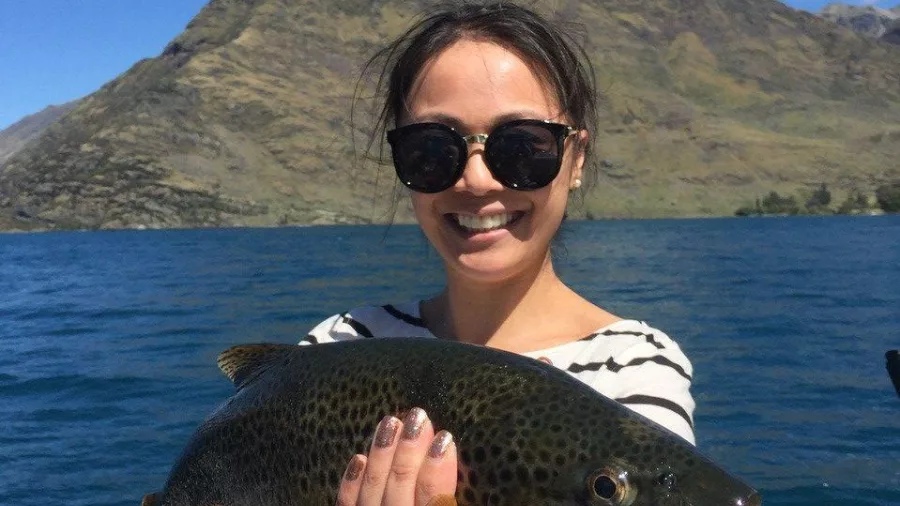 Smiling woman holding a brown trout with Queenstown’s mountains behind