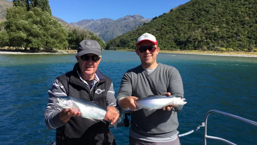 Two men holding freshly caught trout on a fishing boat on Lake Wakatipu