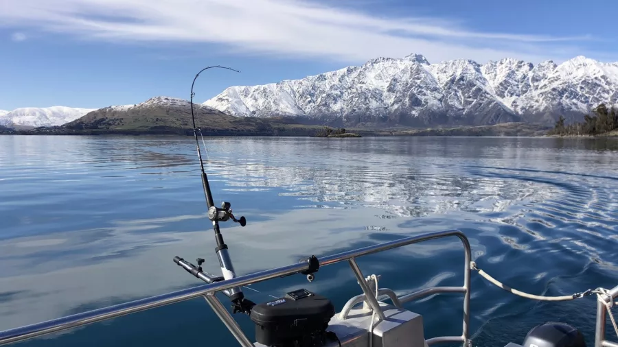 Fishing rod setup on a boat with calm Lake Wakatipu waters and The Remarkables in the background