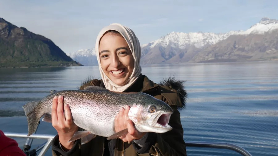 Woman holding a rainbow trout with Lake Wakatipu and snow-capped peaks in the background