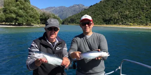 Two men holding freshly caught trout on a fishing boat on Lake Wakatipu
