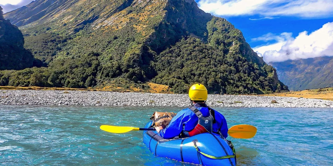 Solo paddler navigating a scenic river in Mount Aspiring National Park surrounded by cliffs and native forest