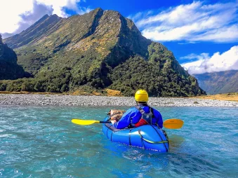 Solo paddler navigating a scenic river in Mount Aspiring National Park surrounded by cliffs and native forest