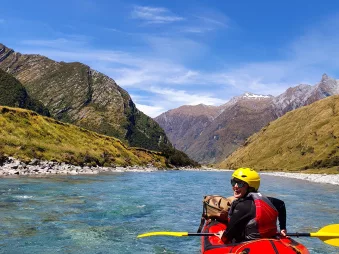 Packrafter on a red raft drifting through clear alpine waters in Mount Aspiring National Park