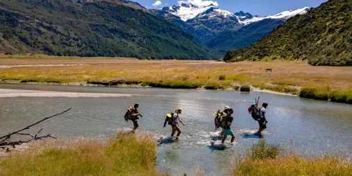 Adventurers hiking across a river in Rees Valley during a packrafting expedition
