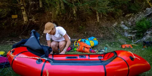 Packrafter preparing gear and raft near the forest in Rees Valley
