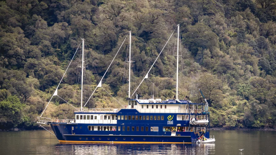 Side view of the Fiordland Navigator with forested cliffs in the background