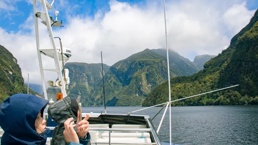 People in raincoats photographing steep cliffs and misty peaks from a boat in Doubtful Sound’s Patea Arm