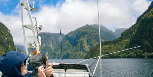 People in raincoats photographing steep cliffs and misty peaks from a boat in Doubtful Sound’s Patea Arm