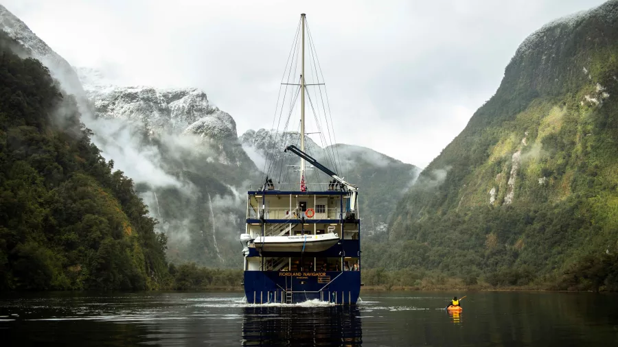 Fiordland Navigator anchored in Doubtful Sound with a kayaker in calm, misty water
