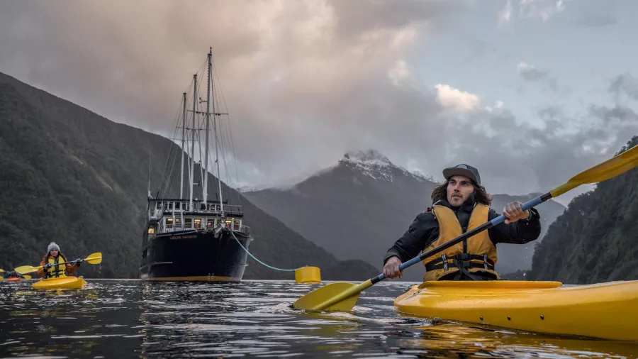 Couple kayaking on Doubtful Sound with the Fiordland Navigator behind them