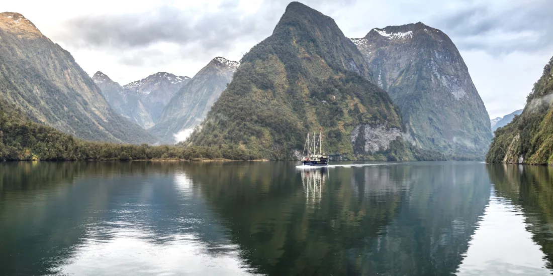 Fiordland Navigator cruise ship reflected in the calm waters of Doubtful Sound surrounded by steep forested peaks
