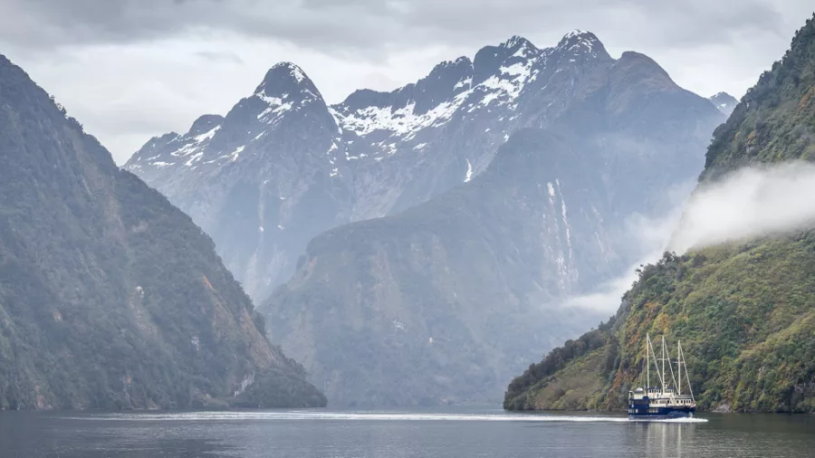 Fiordland Navigator sailing towards snow-capped mountains in Doubtful Sound with mist trailing along the slopes