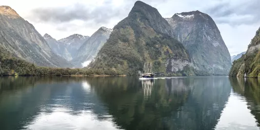 Fiordland Navigator cruise ship reflected in the calm waters of Doubtful Sound surrounded by steep forested peaks