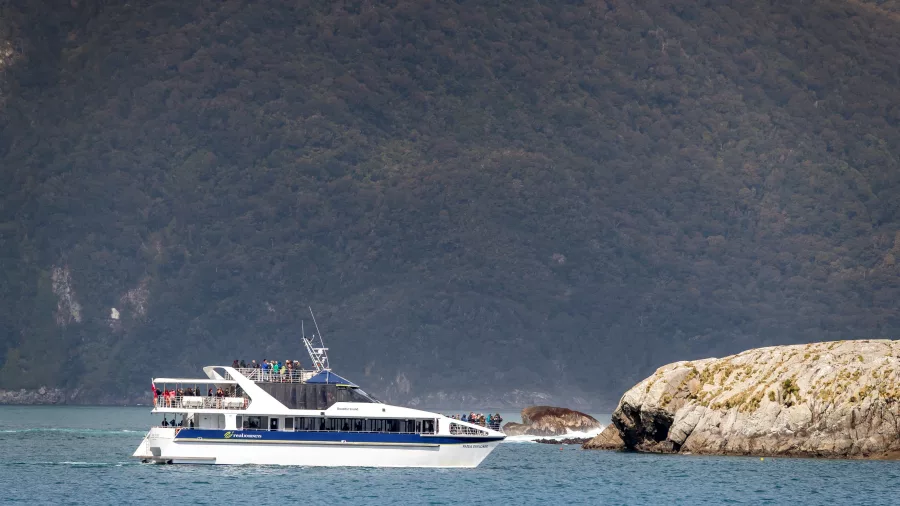 Patea Explorer cruise boat passing a rocky outcrop in Doubtful Sound with forested hills in the background