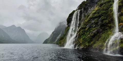 Cascading waterfalls on a rainy day in Doubtful Sound, surrounded by cliffs and mist