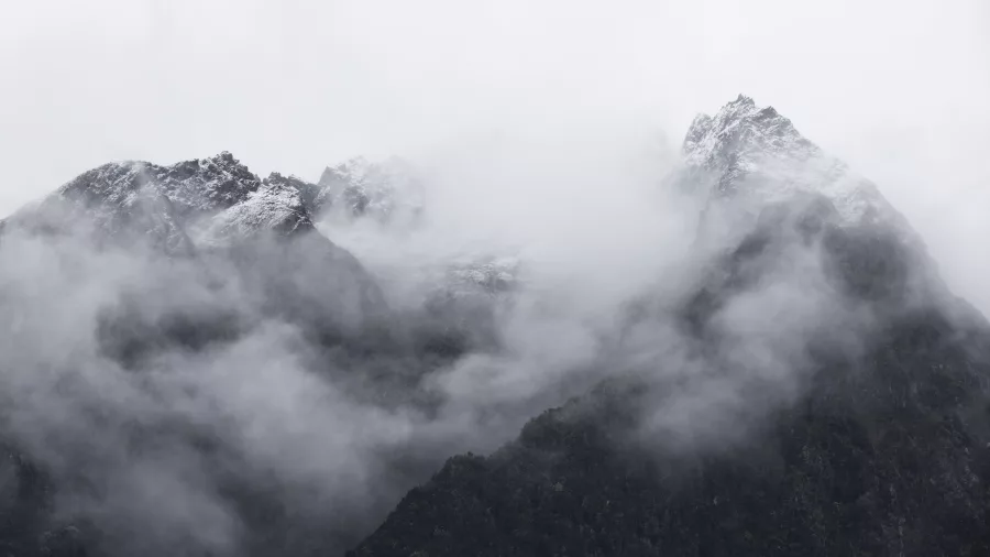 Snow-capped mountain peaks in Fiordland partially covered by thick cloud