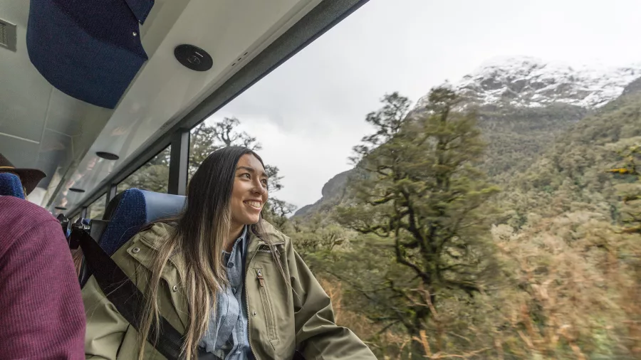 Woman smiling while looking out of the coach window at snow-capped peaks on Wilmot Pass