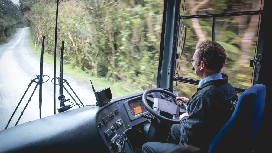 Coach driver steering through forested road on Wilmot Pass