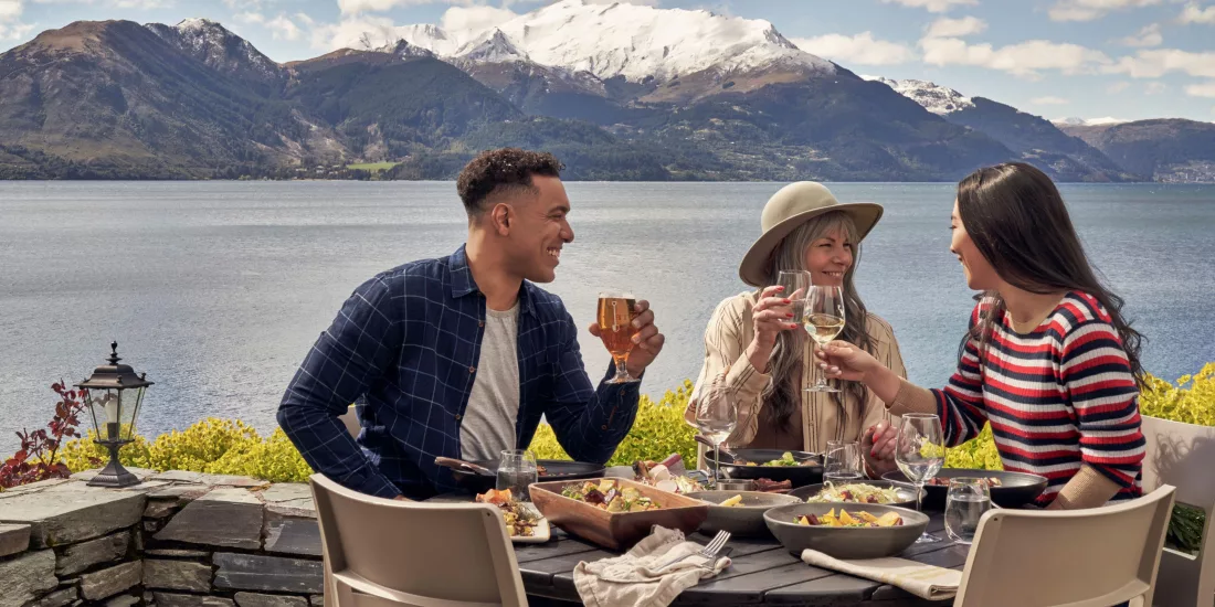 Friends dining outdoors with a stunning lake and mountain view at Walter Peak