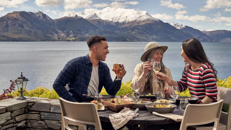 Friends dining outdoors with a stunning lake and mountain view at Walter Peak