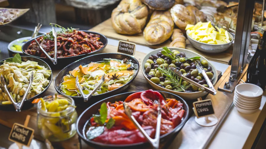 Colourful salad bar featuring olives, capsicum, marinated vegetables, and breads