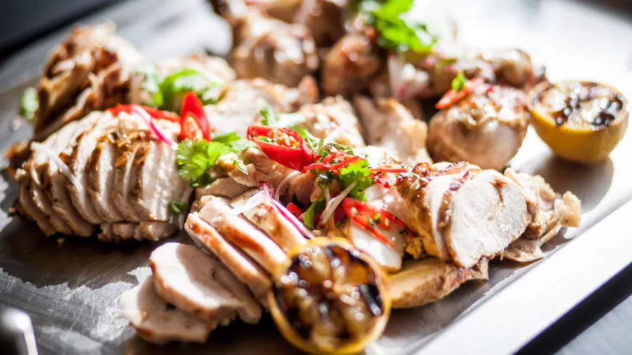Sliced BBQ chicken breast with herbs, lemon, and chilli garnish