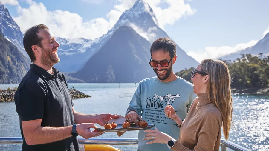 Guests sharing canapés on deck with Mitre Peak in the background