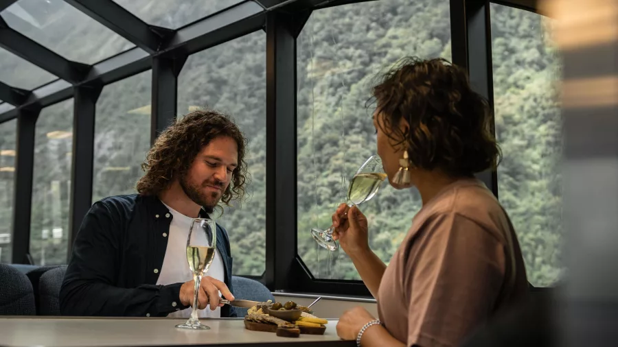 Couple enjoying cheese and wine inside glass-roof lounge on Milford Sound tour