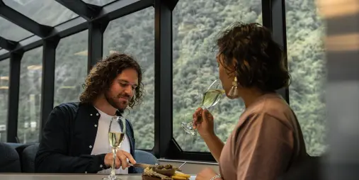 Couple enjoying cheese and wine inside glass-roof lounge on Milford Sound tour