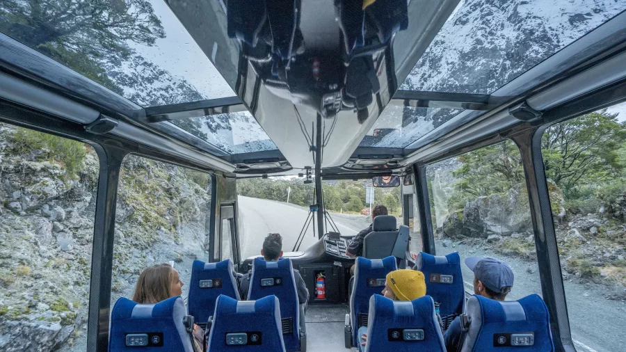 Passengers in a glass-roof coach enjoying mountain views en route to Milford Sound