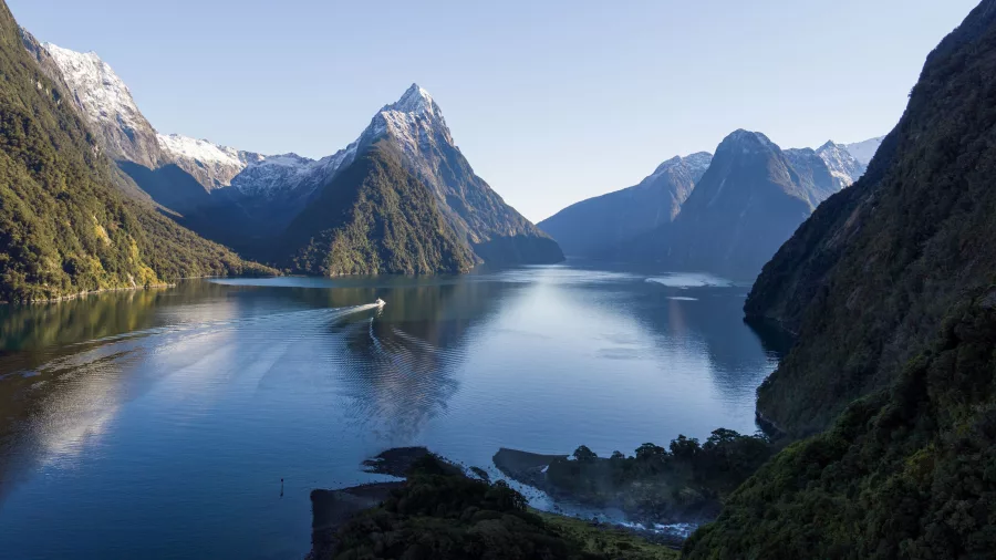 Wide view of Milford Sound with boat cruising through the fiord and dramatic mountain backdrop