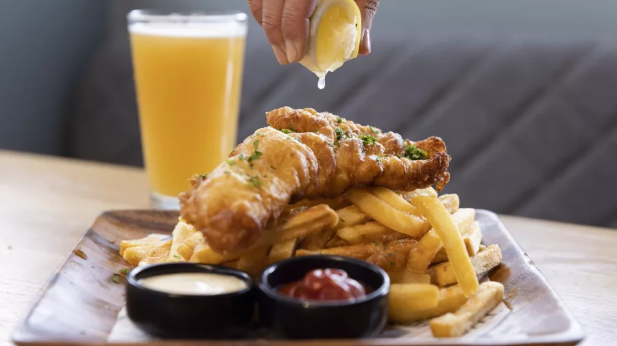 Hand squeezing lemon over fish and chips served with sauce and beer aboard Milford Haven