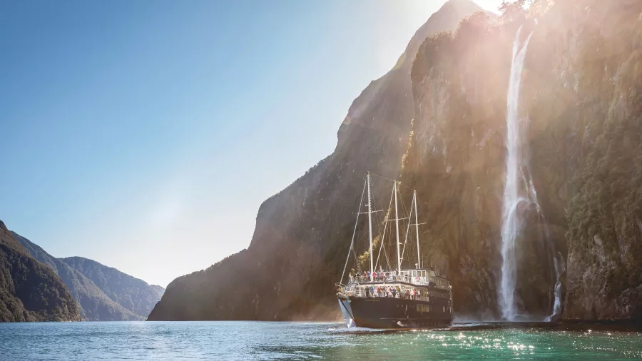 Milford Mariner sailing past Stirling Falls with sunbeams in Milford Sound