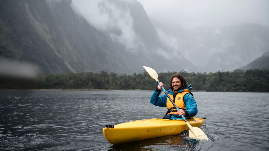 Man kayaking in Milford Sound with misty cliffs in the background