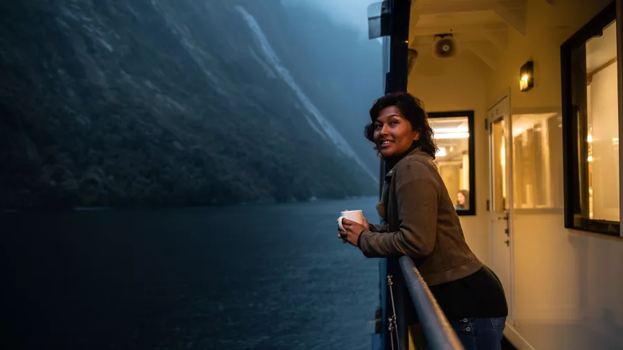 Woman enjoying a warm drink on the balcony of Milford Mariner in Milford Sound
