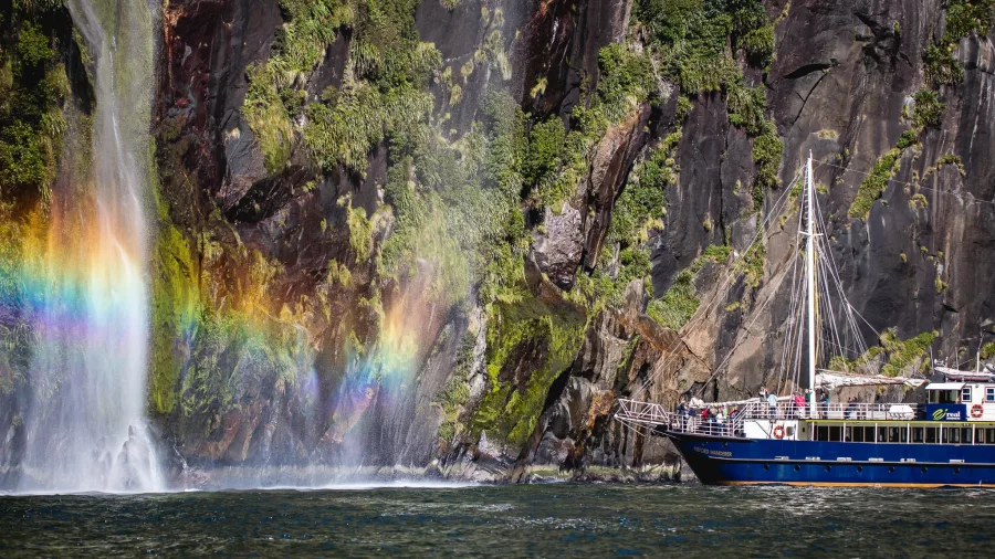 Milford Mariner near a waterfall with rainbow mist in Milford Sound