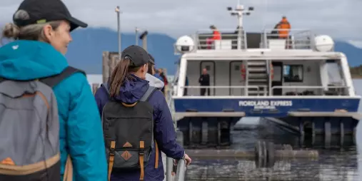 Hikers approaching the Fiordland Express, Milford Track Water Taxi, at the dock, ready for their journey.