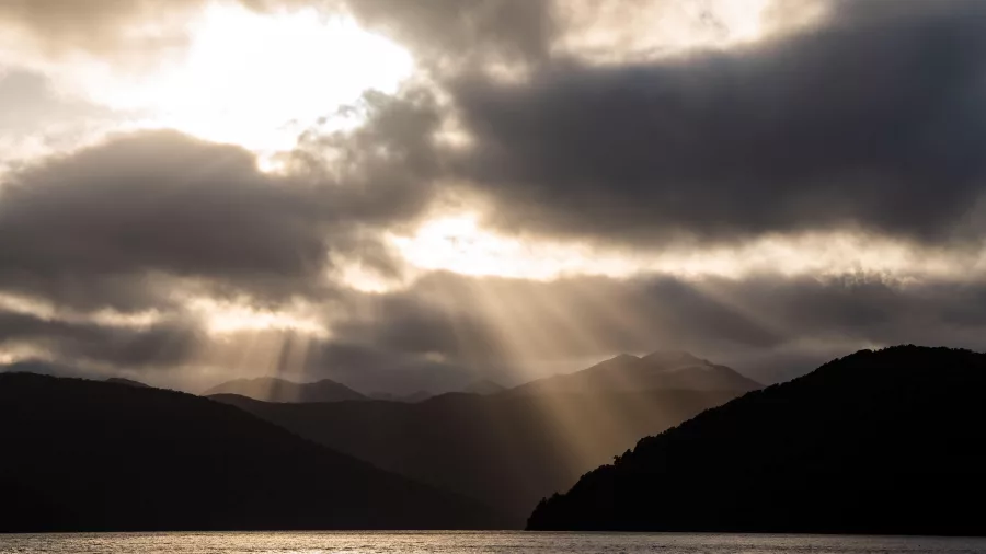 Beams of sunlight breaking through dramatic cloud cover over the Fiordland coastline