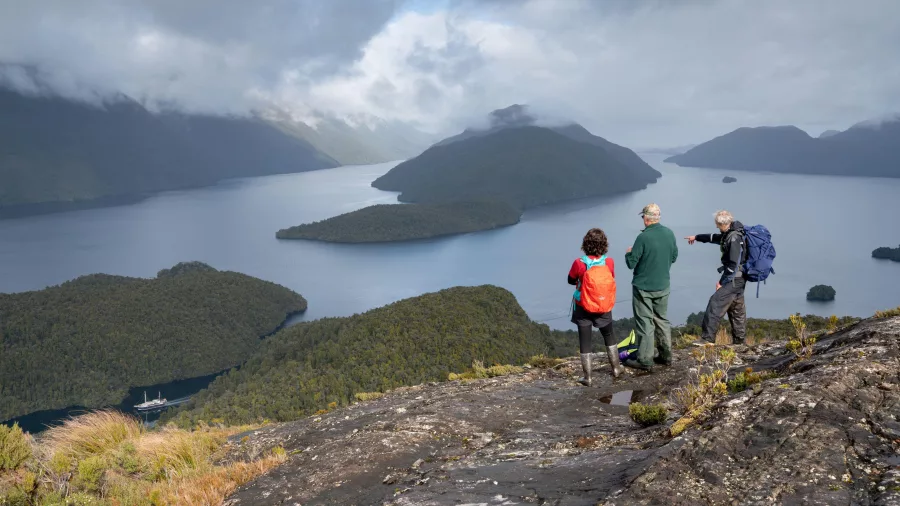 Group of hikers enjoying a spectacular view over Preservation Inlet and forested islands from a high rocky ledge