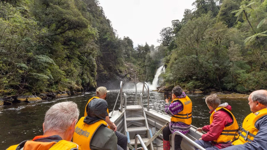 Guests in a small boat cruising close to a powerful waterfall deep in Fiordland