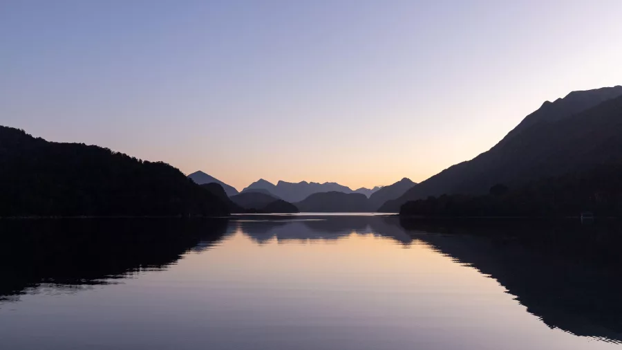 Tranquil twilight over still water surrounded by silhouetted mountains in Fiordland