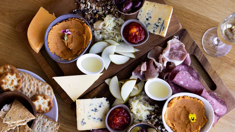 Cheese, cured meats, crackers, and fruits served on a wooden platter with wine aboard the Spirit of Queenstown Lake Cruise.