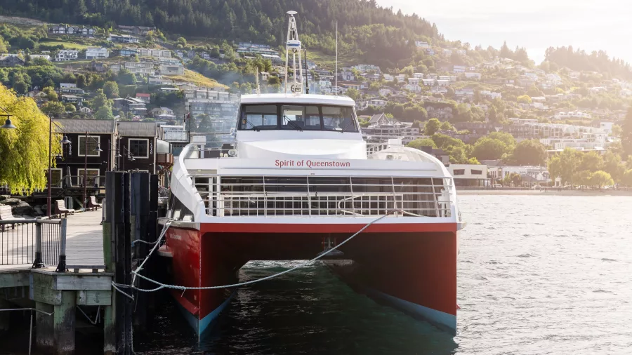 Spirit of Queenstown docked at the pier in Queenstown with a scenic mountain backdrop.