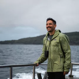 A smiling passenger aboard the Stewart Island ferry on a scenic journey, with coastal views in the background.
